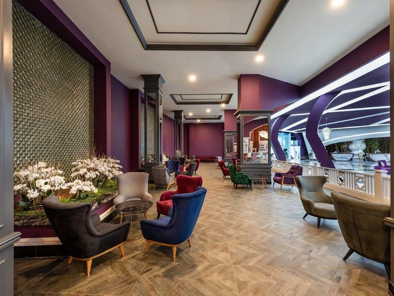 Moderní hotelová lounge s barevnými křesly a fialovými akcenty.