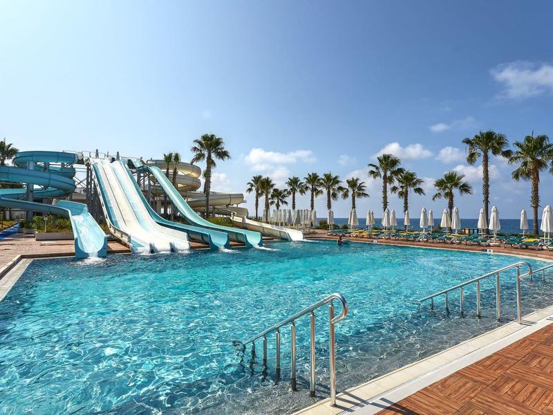 Velký bazén s vodními skluzavkami a palmami na slunné dovolené.