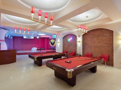 Sala giochi con tavoli da biliardo, panno rosso e illuminazione moderna in uno spazio elegante.