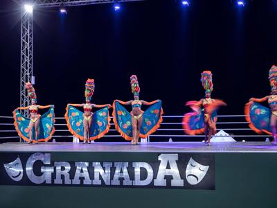 Cinque ballerini in costumi colorati si esibiscono sul palco di notte.