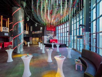 Světelná konferenční místnost s velkými okny, bílými vysokými stoly a zavěšenou výzdobou.