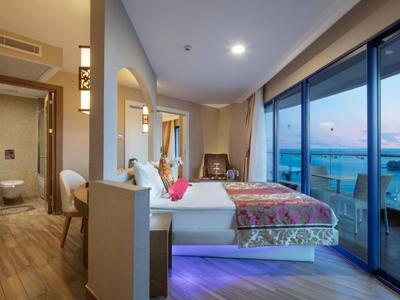 Modernes Schlafzimmer mit Doppelbett, Holzfußboden, Zugang zum Balkon und Meerblick bei Sonnenuntergang.