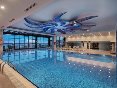 Prostorný vnitřní bazén s velkými okny a moderní stropní dekorací.