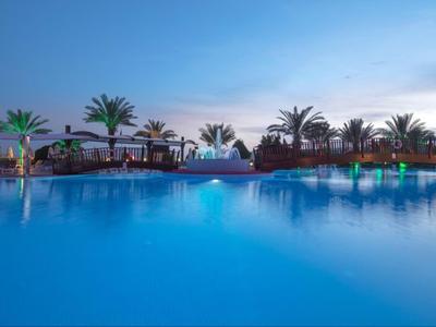 Grande piscina dell'hotel con illuminazione e palme al tramonto
