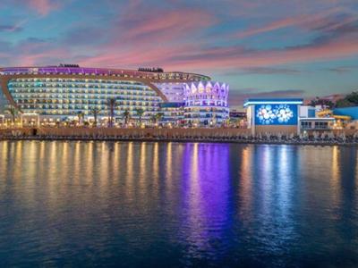 Noční pohled na rušné nábřeží s osvětlenými budovami a odrazy ve klidné vodě.