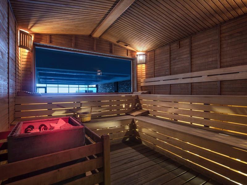 Interiér dřevěné sauny s tlumeným osvětlením a velkým panoramatickým oknem.
