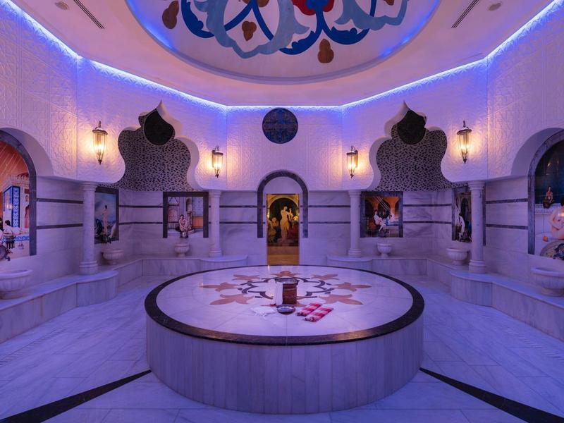 Interiér hammamu s jemným fialovým světlem a kruhovou centrální vanou.