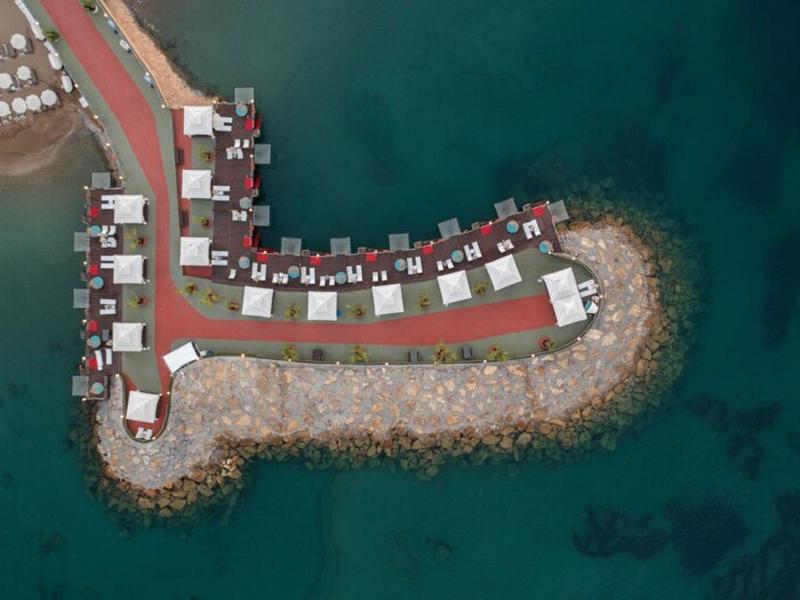 Letecký pohled na mol s bílými kabinkami na červené cestě nad modrou vodou.