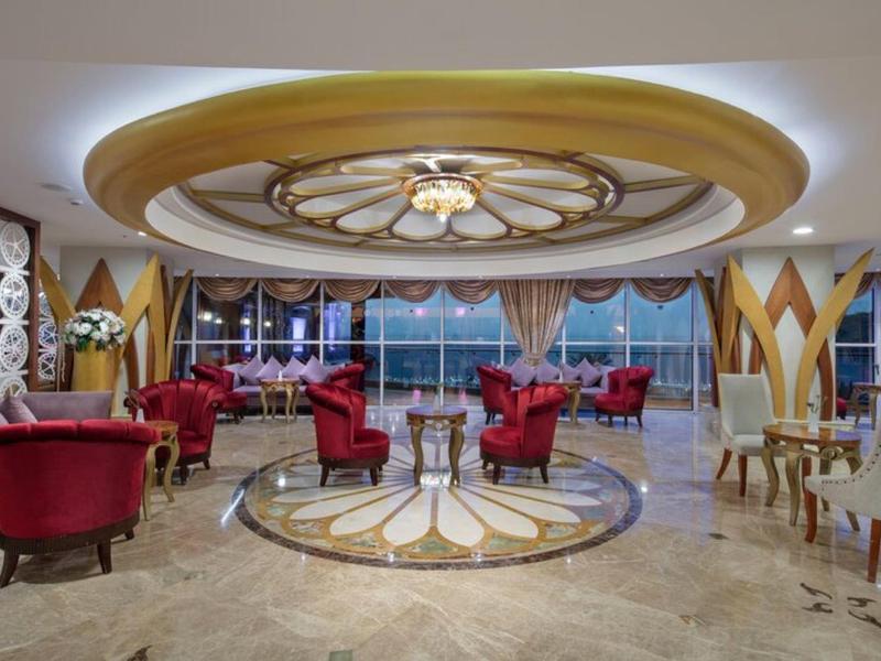 Luxusní hotelový salonek s červenými křesly a velkými okny s výhledem na moře.