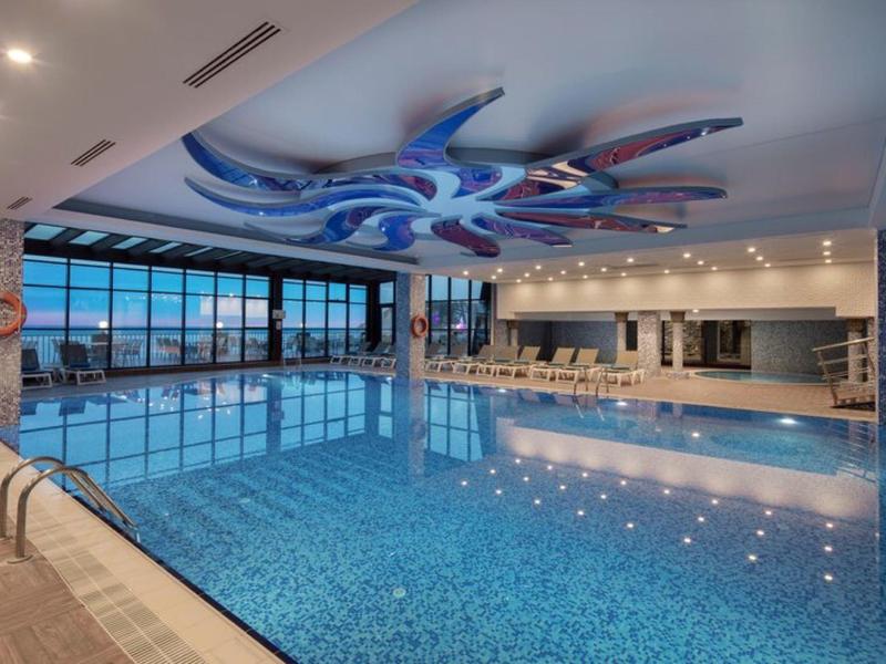 Prostorný vnitřní bazén s velkými okny a moderní stropní dekorací.