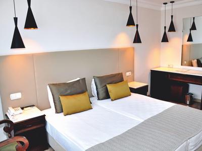 Hell eingerichtetes Hotelzimmer mit Doppelbett, Nachttischen, Pendelleuchten und großem Spiegel.