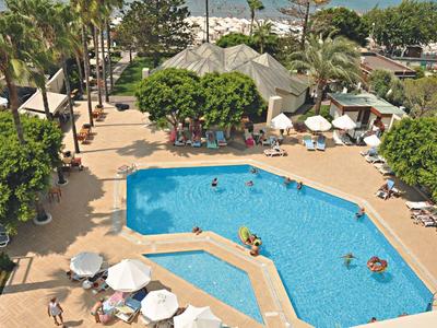 Großer blauer Pool mit Menschen, umgeben von Sonnenschirmen, Liegen und Palmen in sonniger Lage.