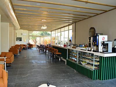 Salon d'hôtel moderne avec grandes fenêtres, bancs et long comptoir vert.