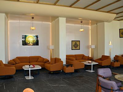 Salon d'hôtel moderne avec canapés orange, tables rondes et œuvres d'art aux murs.