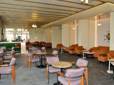 Un salon d'hôtel élégant avec des fauteuils confortables et des tables, design moderne et luminaires au plafond.