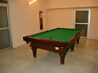 Table de billard avec tissu vert dans une pièce lumineuse et simple avec un sol en marbre.