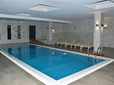 Espace intérieur avec une piscine rectangulaire et des chaises longues dans un hôtel.