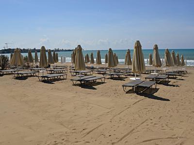 Plage de sable vide avec des rangées de transats et parasols fermés sous un ciel bleu.