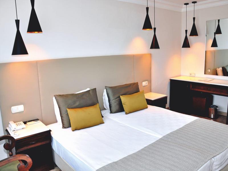 Modernes Hotelzimmer mit Doppelbett, Nachttischen, Hängelampen und Spiegelschreibtisch