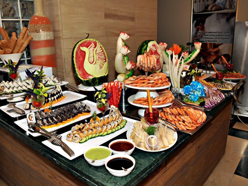 Buffet mit vielfältigem Seafood, rotem und grünem Gemüse, Saucen und dekorativen Früchten.