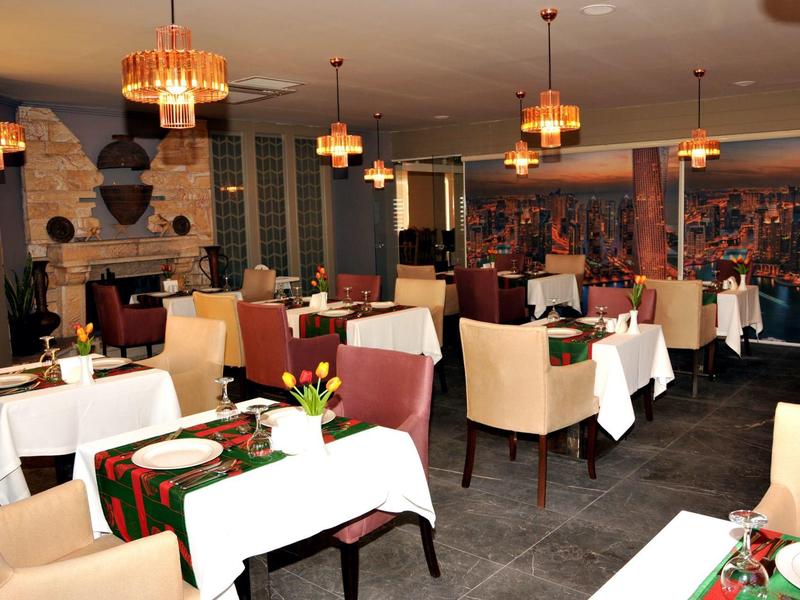 Gemütlicher Restaurantraum mit weißen Tischdecken, bequemen Sesseln und warmen Lampen an der Decke.