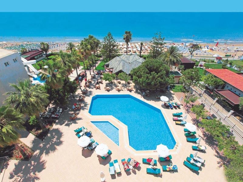 Großer blauer Pool mit Liegestühlen und Sonnenschirmen, Palmen und Strand im Hintergrund.