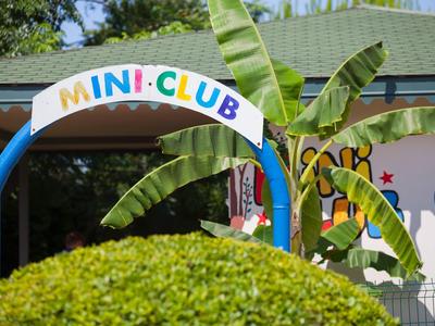 Vstup do dětského klubu s barevným nápisem, obklopený rostlinami.