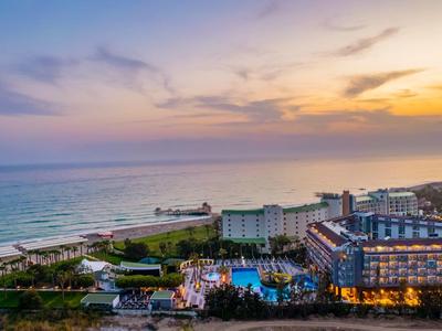 Hotelový komplex s bazénem a výhledem na moře při západu slunce.