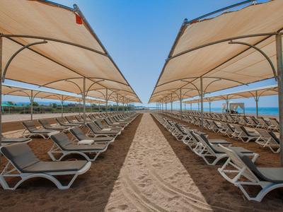 Symmetrisch angeordnete Liegestühle und Sonnenschirme am Strand unter blauem Himmel.