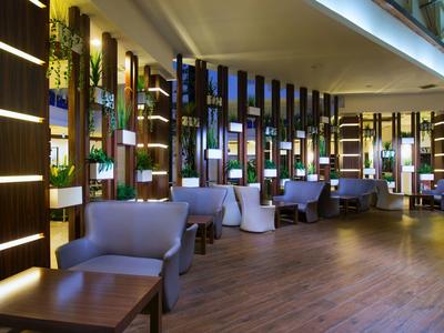 Moderní hotelová lounge s modrými křesly, dřevěnou podlahou a vertikálními zelenými stěnami.