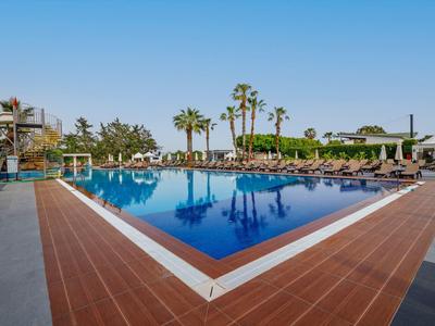 Velký venkovní bazén s lehátky a palmami pod jasně modrou oblohou.