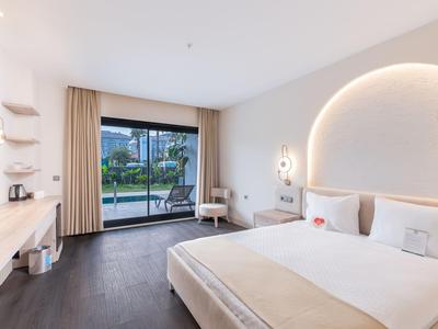 Camera d'hotel moderna con letto matrimoniale, area salotto e vista sulla piscina attraverso grandi finestre.