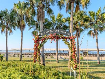 Luk s květinovou dekorací před palmami a pobřežní promenádou pod slunečnou oblohou.