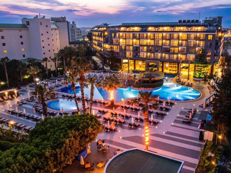 Hotel s osvětleným bazénem a lehátky při západu slunce.