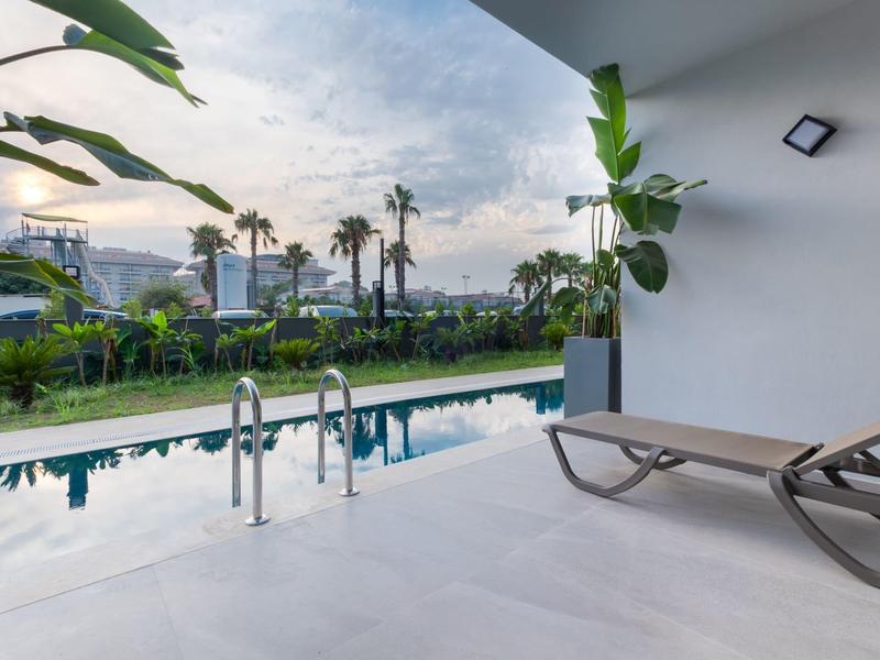 Moderní balkon s výhledem na bazén, lehátky a tropické rostliny