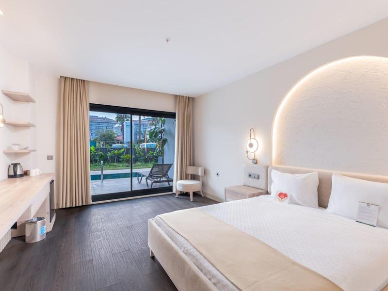 Světý moderní hotelový pokoj s manželskou postelí, balkonem a výhledem na bazén a zahradu.