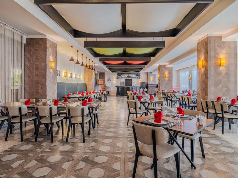 Prostorná restaurace s mnoha stoly, dekorativními stropními panely a teplým osvětlením.