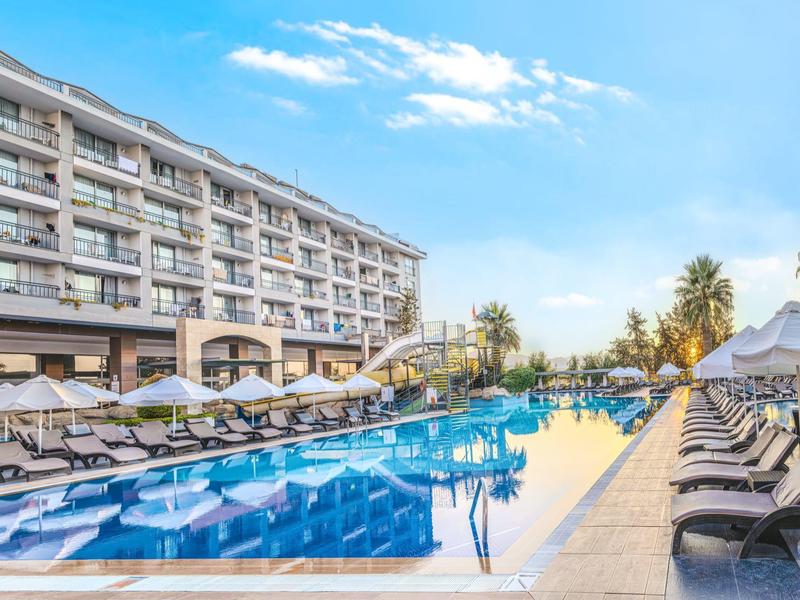 Moderní hotel s dlouhým venkovním bazénem, lehátky a slunečníky pod jasnou oblohou