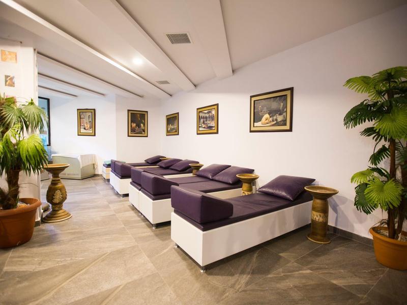 Moderní odpočinková místnost s lehátky, rostlinami a dekorativními obrazy na stěnách.