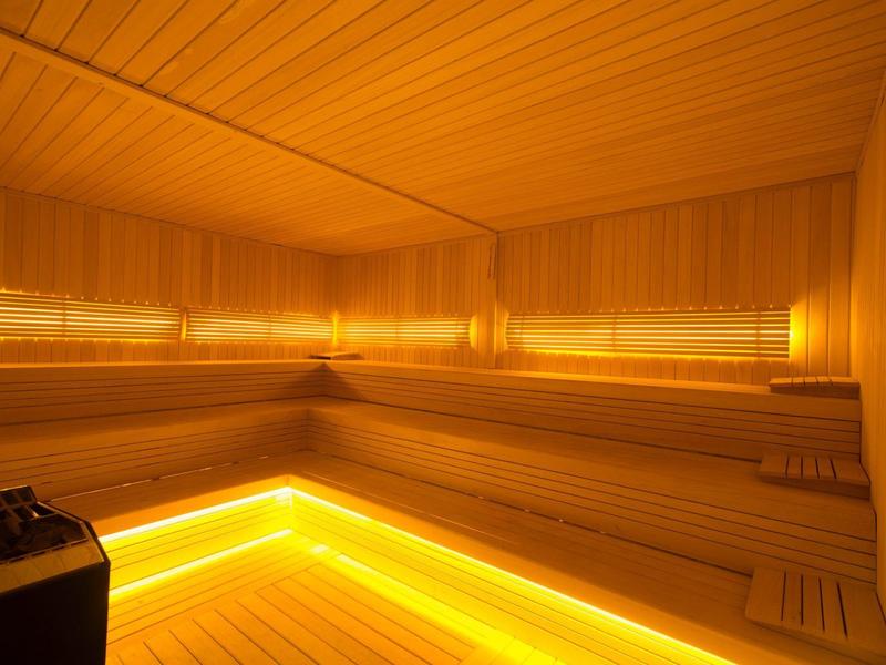 Jasná finská sauna s dřevěnými lavicemi a nepřímým LED osvětlením pod sedadly.