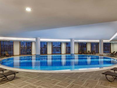 Groot rond binnenzwembad met ligstoelen en panoramische ramen in een moderne omgeving.