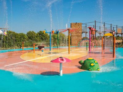 Kleurrijke waterspeelplaats met waterstralen en klimrek op een zonnige dag.