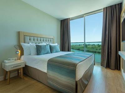 Modern hotelkamer met groot bed, nachtkastje en groot raam met uitzicht op de natuur.