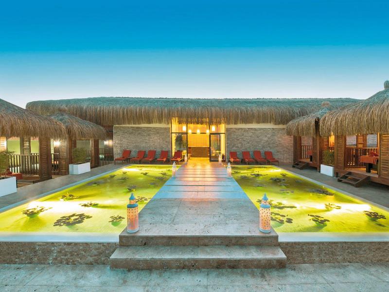 Symmetrisch hotelzwembad met zitgedeeltes en tropisch dak onder heldere lucht.