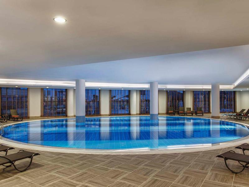 Groot rond binnenzwembad met ligstoelen en panoramische ramen in een moderne omgeving.