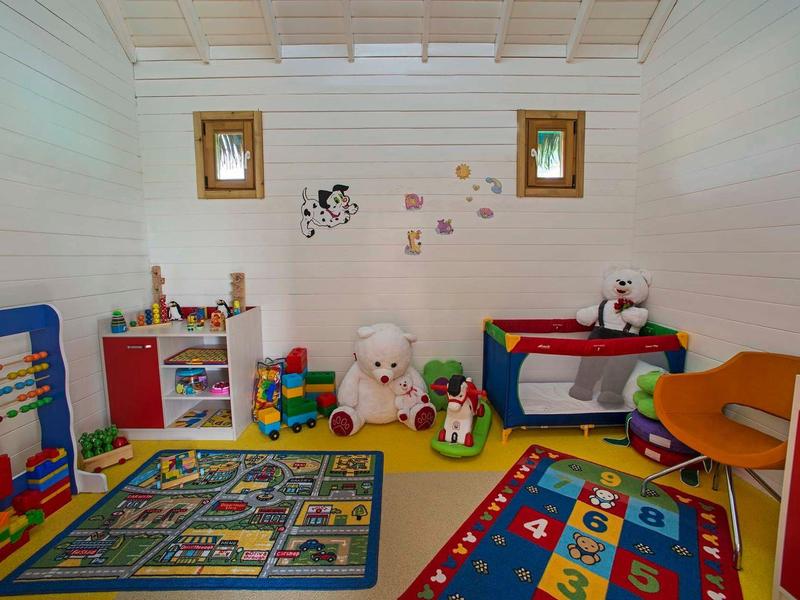 Kleurrijke speelkamer voor kinderen met speelgoed, vloerkleden en twee kleine ramen.