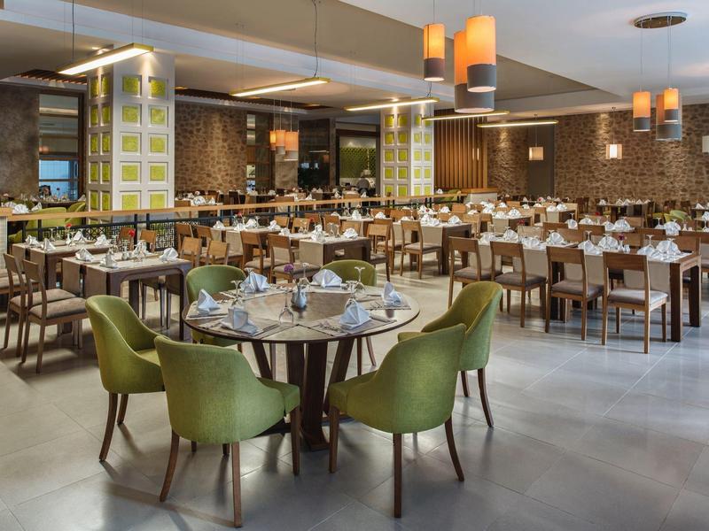 Grote, lichte eetzaal met moderne groene stoelen en veel gedekte ronde tafels.