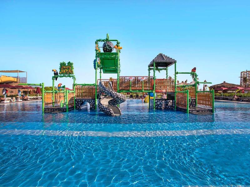 Waterpark met spelletjes en glijbanen in een groot zwembad bij heldere lucht.