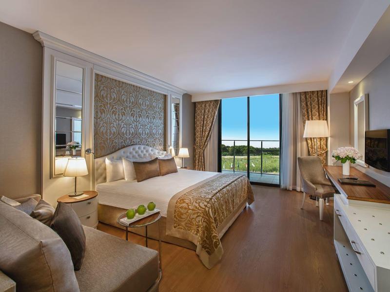 Elegant hotelkamer met groot bed, bank, bureau en uitzicht op groene omgeving.