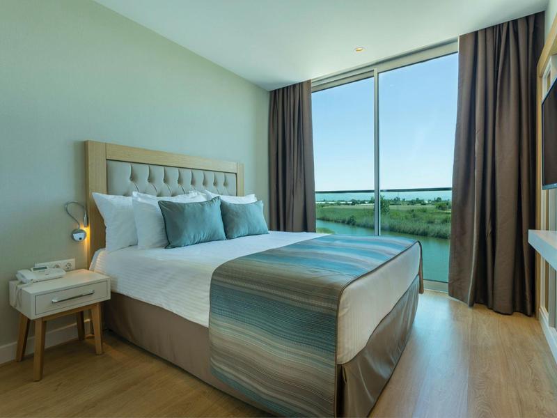 Modern hotelkamer met groot bed, nachtkastje en groot raam met uitzicht op de natuur.